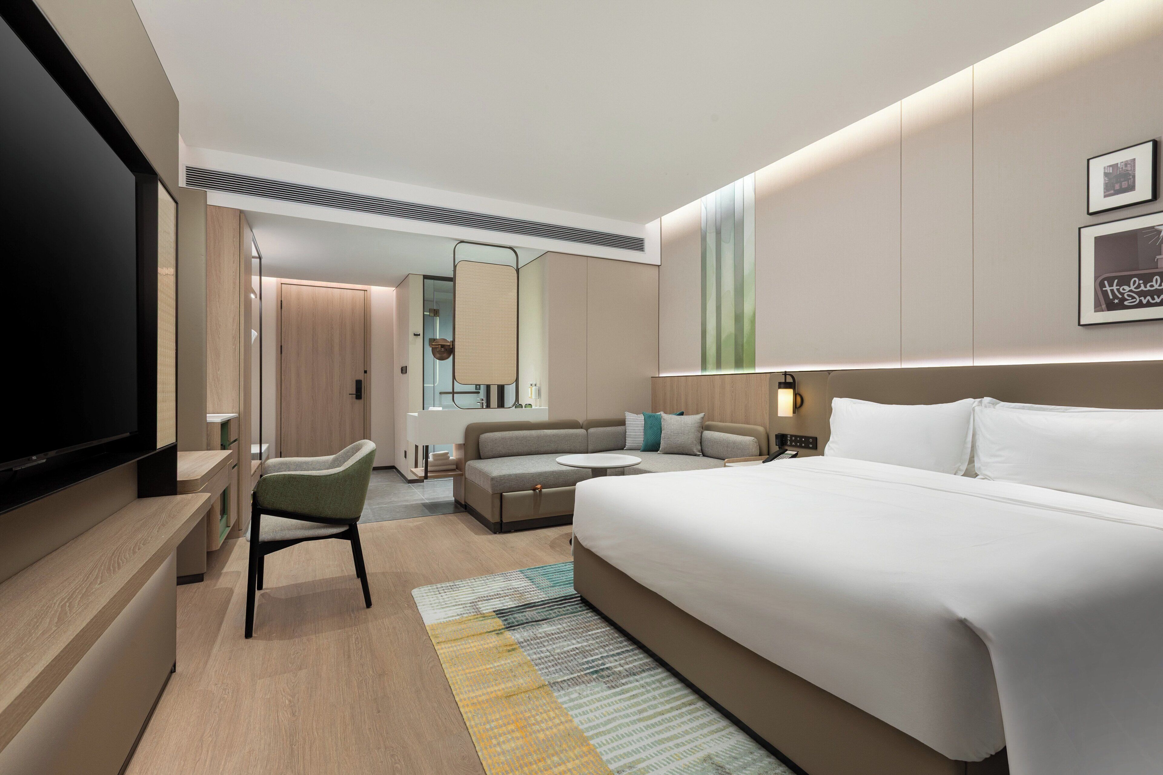 Une chambre d’hôtel moderne dotée d’un grand lit, d’une télévision à écran plat, d’un canapé, d’un bureau et d’un miroir.