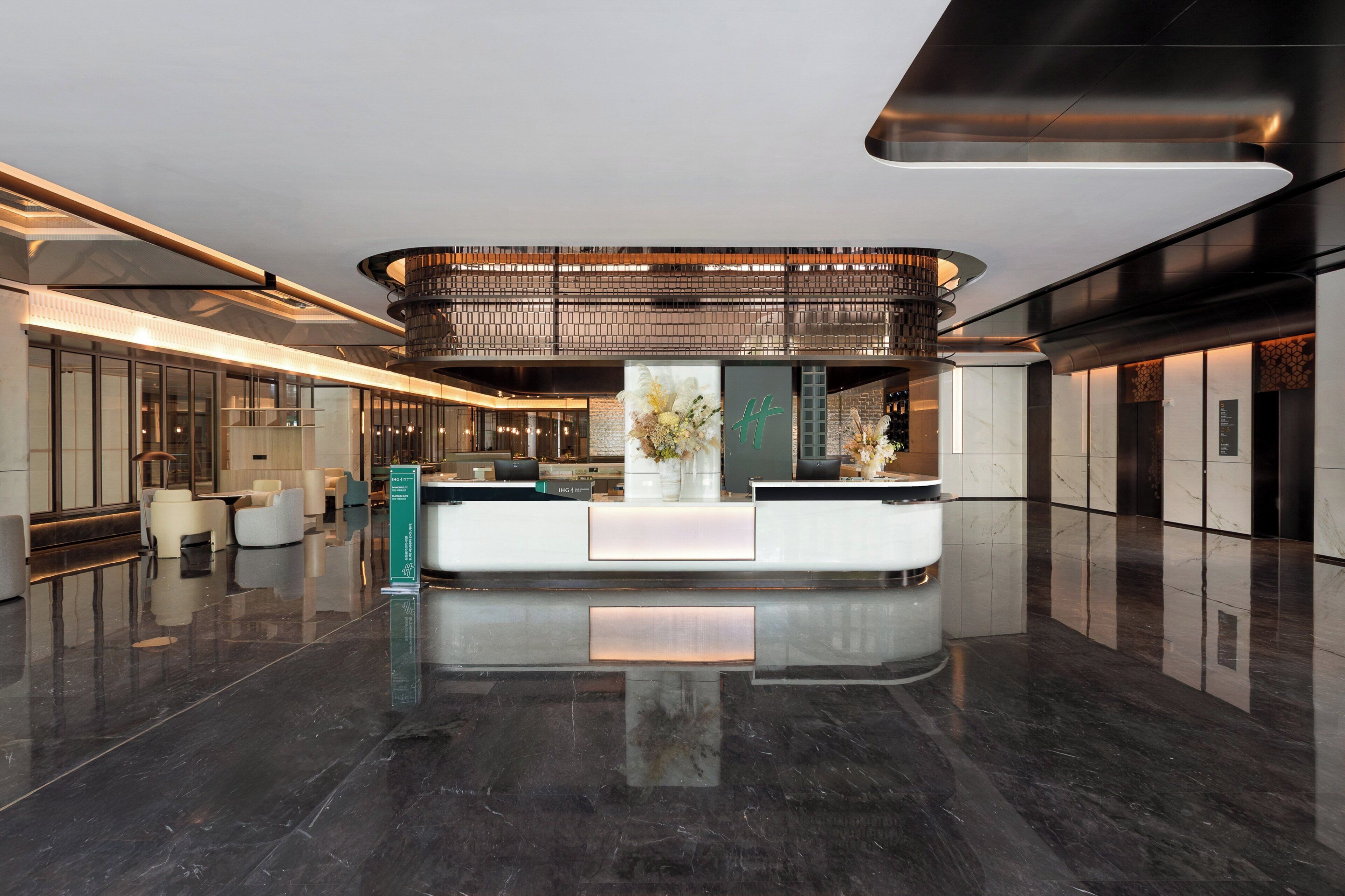 Un hall d’hôtel moderne comprenant un comptoir d’accueil, un espace salon et une plante décorative placée au centre.