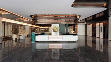 Un hall d’hôtel moderne comprenant un comptoir d’accueil, un espace salon et une plante décorative placée au centre.