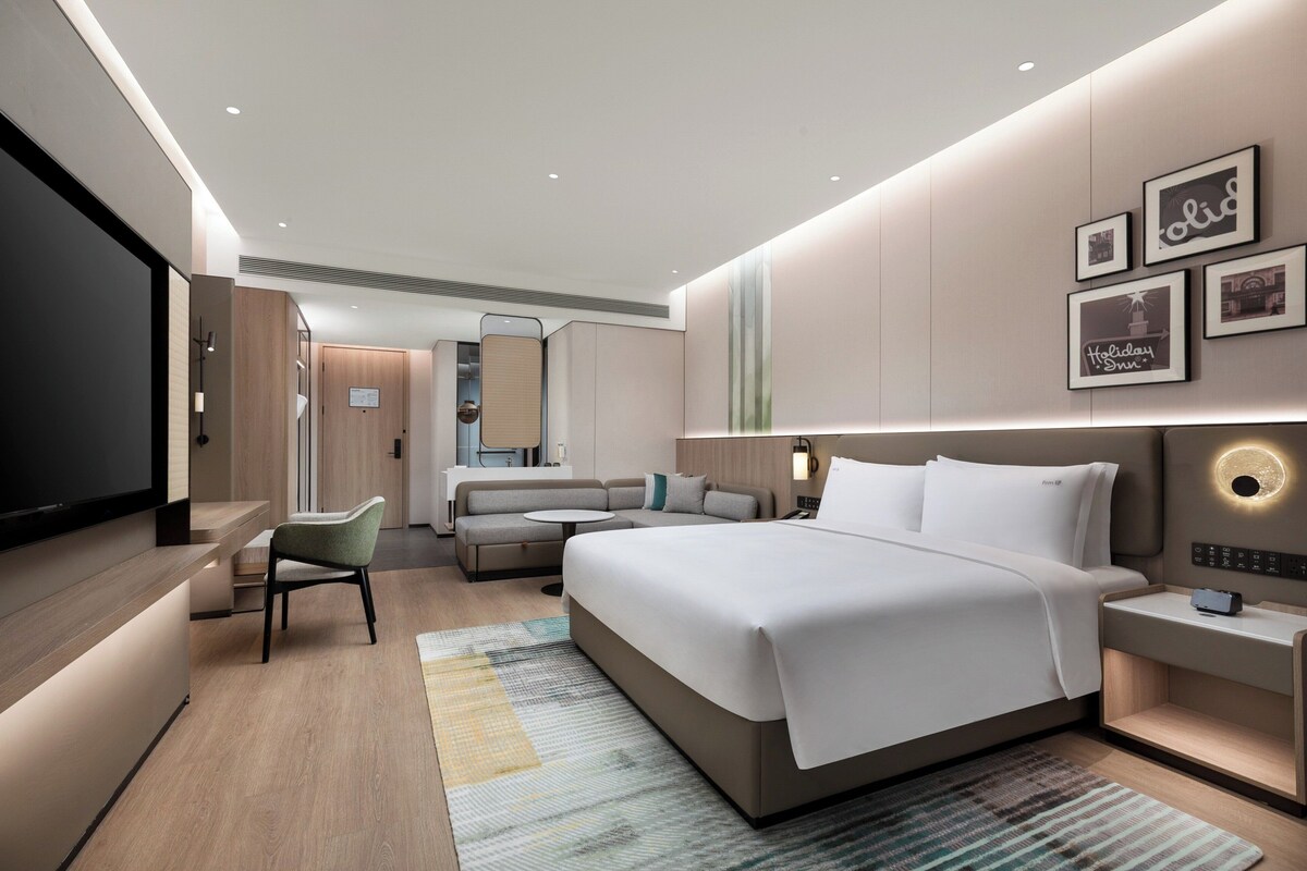 A modern hotel room with a large bed, a sofa, a desk, and a TV.