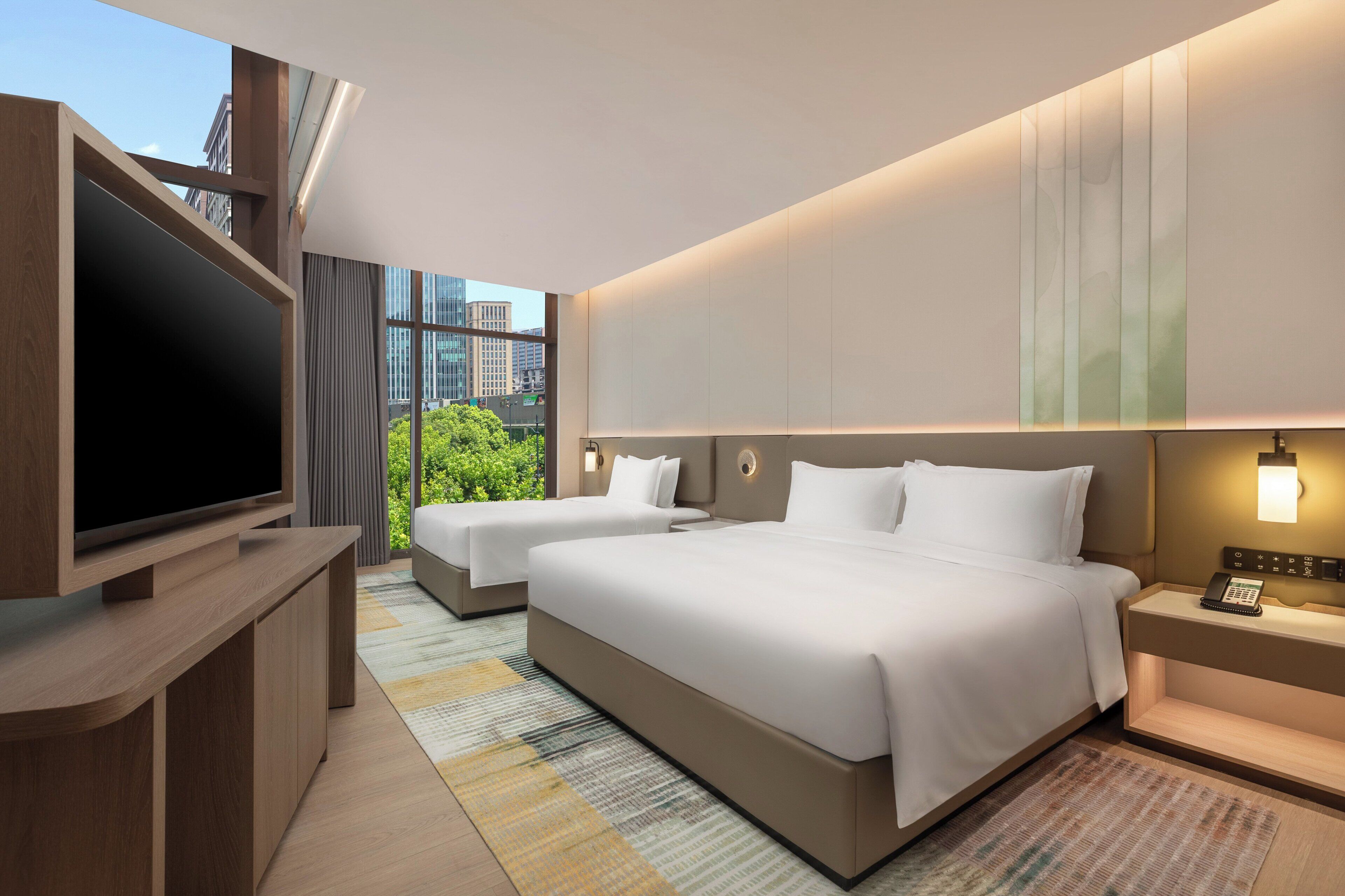 A modern hotel room with two beds, a flat-screen TV, and a city view.