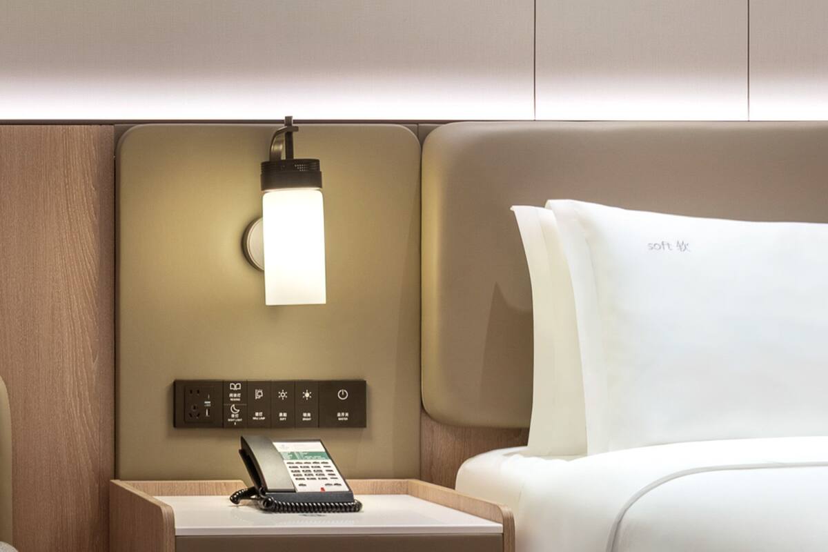 A modern hotel room with a bedside table, a lamp, a phone, and a bed with white bedding.