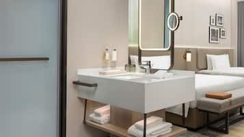 A modern hotel room with a large bed, a bedside table, a vanity with a mirror, and a small seating area.