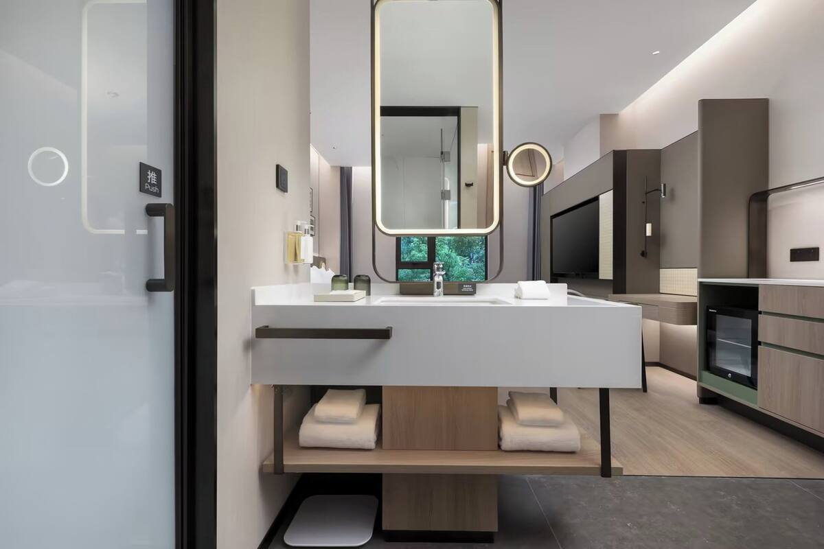 A modern bathroom with a large mirror, a sink, and a toilet. There is a television and a cabinet in the background.