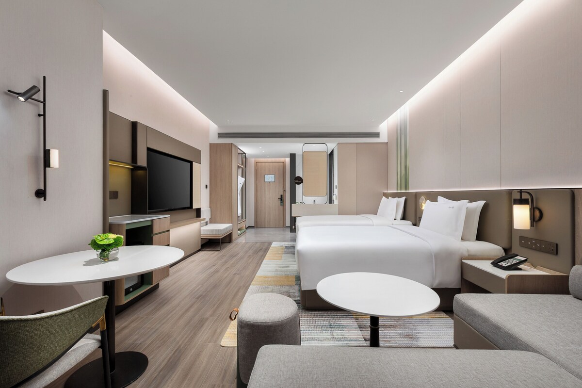 A modern hotel room with a large bed, a desk, a TV, and a small dining area.