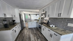 A modern kitchen with white cabinets, granite countertops, and a central island. - Seabreeze - Charming 2-bedroom house in amazing Holiday with WiFi, AC.  (Holiday)