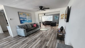 A spacious living room with a grey sofa, a glass coffee table, and a dark wooden floor. - Seabreeze - Charming 2-bedroom house in amazing Holiday with WiFi, AC.  (Holiday)