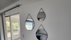 A room with a sliding glass door leading to a balcony, a white wall with three circular mirrors, and a wooden floor. - Seabreeze - Charming 2-bedroom house in amazing Holiday with WiFi, AC.  (Holiday)