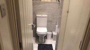 A bathroom with a toilet, a trash bin, and a towel on the floor.