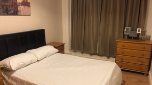 A bedroom with a bed, a nightstand, a dresser, and a painting on the wall.