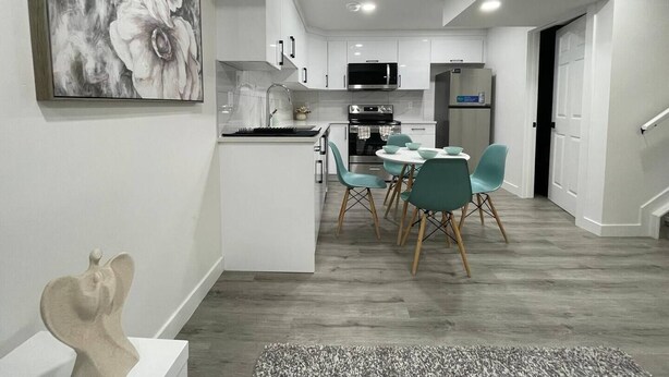 A modern kitchen with white cabinets, a central island, and teal chairs. - Comfy 2BR Basement Getaway (Edmonton)