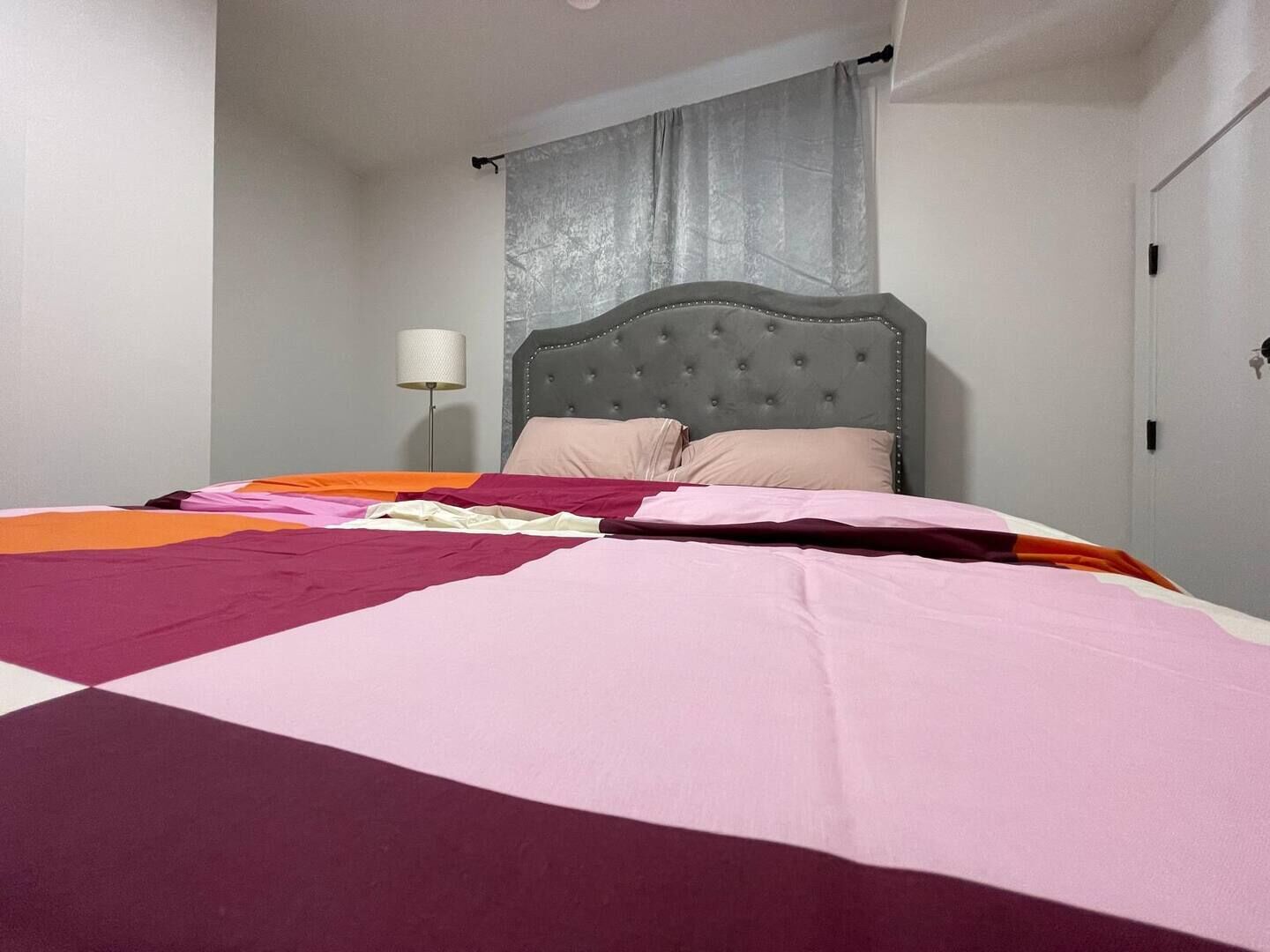 A bedroom with a bed, a headboard, a lamp, and a door.