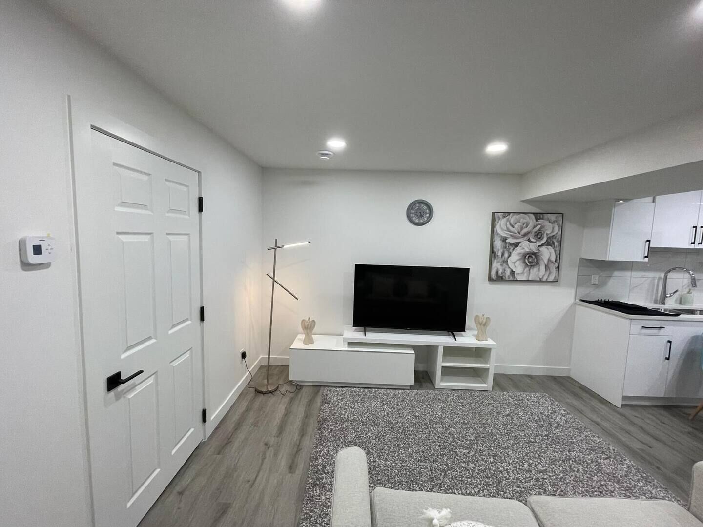 A modern living room with a flat-screen TV, a small white cabinet, and a grey carpet.