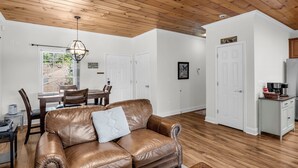 A spacious living room with a brown leather sofa, a dining area with a table and chairs, and a kitchen area with cabinets and a refrigerator.