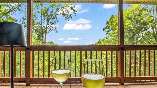 Two glasses of white wine on a table with a wooden deck and a view of trees and sky.