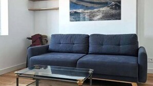Un salon avec un canapé bleu foncé, une table basse en verre et un tableau accroché au mur.