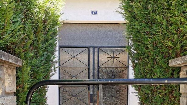 Une entrée fermée par un portail en métal et bordée de murs en pierre, qui mène à un bâtiment portant le numéro 17.