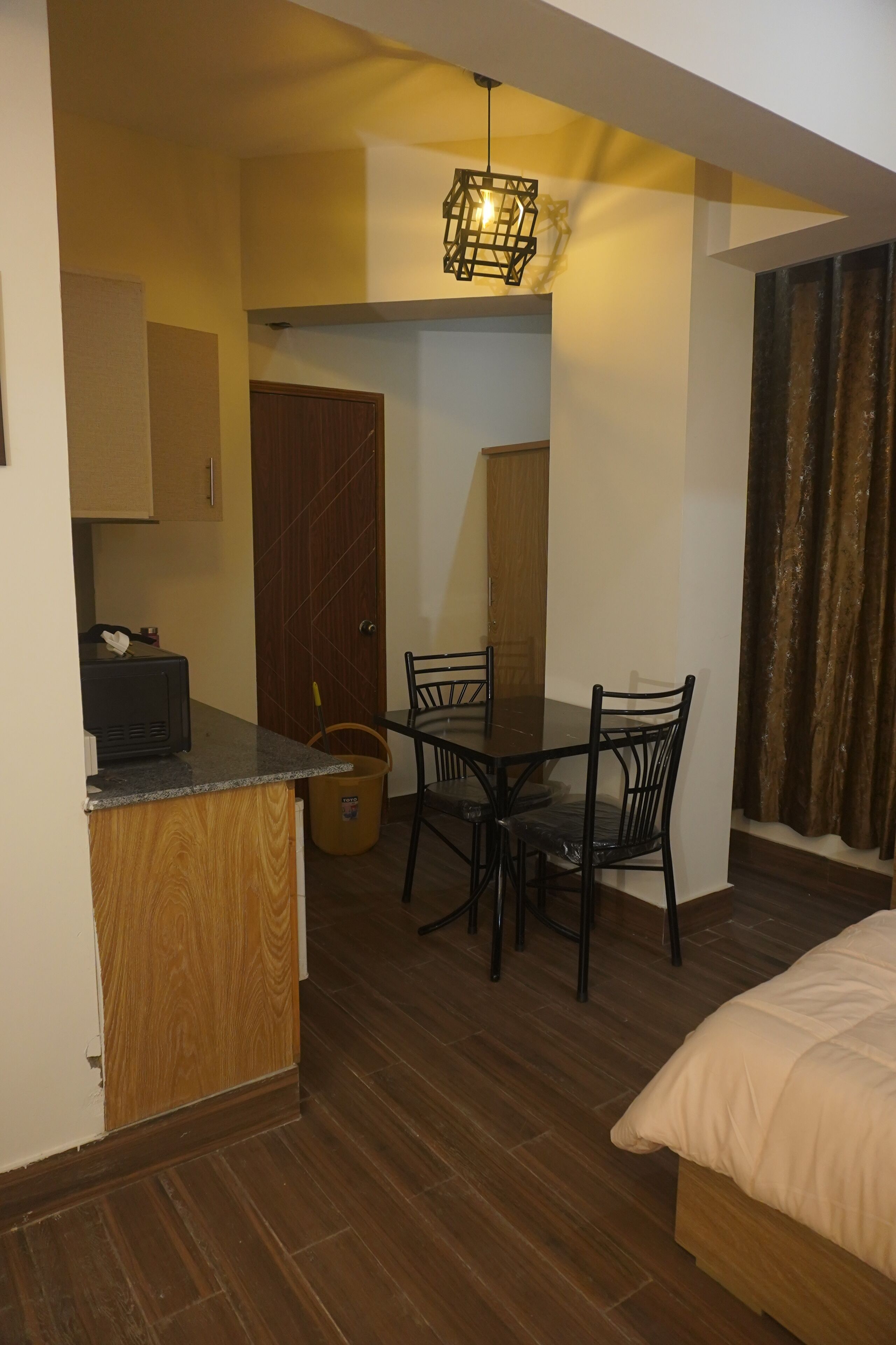 Une pièce de taille modeste comprenant une table à manger en bois, des chaises, un lit, une petite kitchenette et une porte donnant sur une autre pièce.