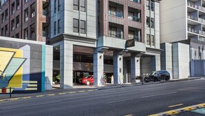 A modern hotel entrance with a prominent 'H' sign, a covered parking area, and a red car parked outside. - Central City Winter Escape HotTub HeatedPool Sauna (Auckland)