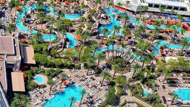 Vista aérea de un resort con varias piscinas, palmeras y tumbonas.
