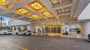 Entrada de hotel de diseño moderno, con puerta de cristal, mostrador de recepción y zona de estacionamiento con automóviles.