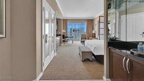 Habitación de hotel con cama, un pequeño escritorio, una silla, ventanal con vistas y kitchenette.