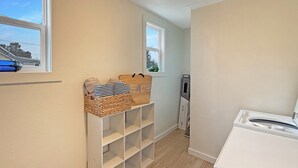 A laundry room with a washing machine, a wicker basket with towels, and a vacuum cleaner. - Welcoming 2-bedroom house 10min walk to the beach in Seaside (Seaside)