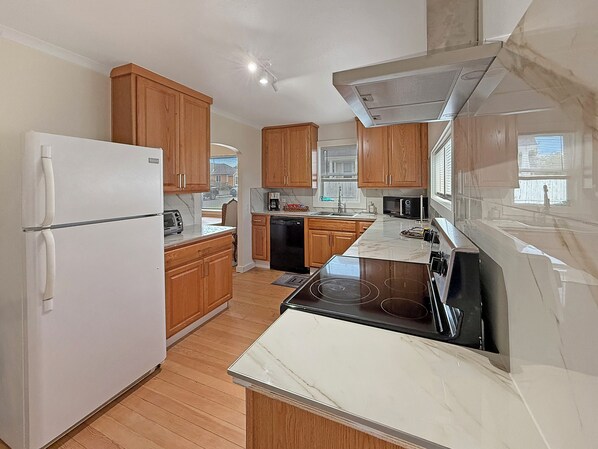 A modern kitchen with wooden cabinets, a white refrigerator, a black dishwasher, and a stainless steel stove.