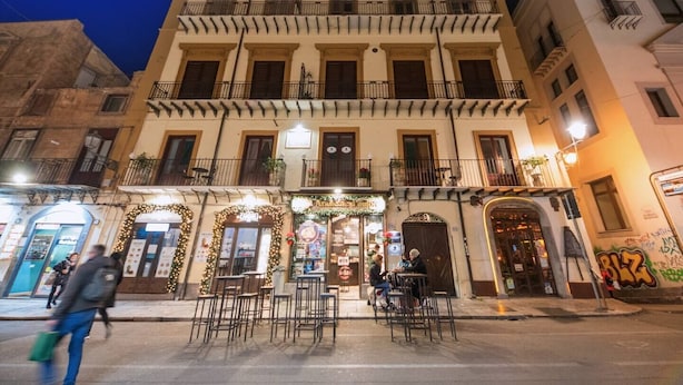 A multi-story building with a ground-floor cafe area featuring outdoor seating. - Casta Diva Luxury Apartments (Palermo)
