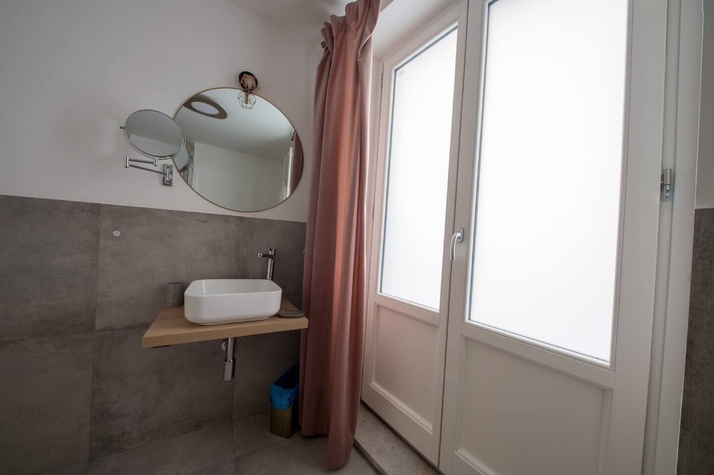 A bathroom with a white sink, a round mirror, and a window with curtains.