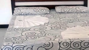 A bed with a patterned bedspread and pillows, a wooden headboard, and a white wall in the background. - Baron Suítes (Ubatuba)