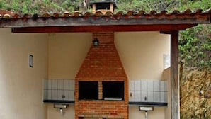 A covered outdoor kitchen area with a brick chimney, two sinks, and a tiled floor. - Baron Suítes (Ubatuba)