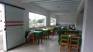 A dining area with tables and chairs, large windows, and a tiled floor. - Baron Suítes (Ubatuba)