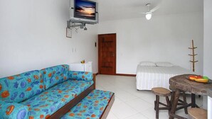 A room with a sofa, a bed, a small table, and a television mounted on the wall. - Baron Suítes (Ubatuba)