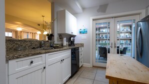 A kitchen with white cabinets, granite countertops, a coffee maker, and a refrigerator.