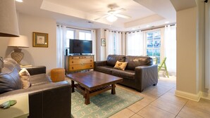 A living room with a sofa, a coffee table, a television on a dresser, and a ceiling fan.