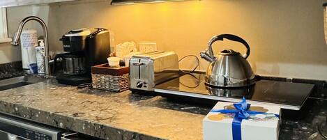A kitchen with a microwave, toaster, kettle, and a dish rack. There is a box with a blue ribbon on the counter.