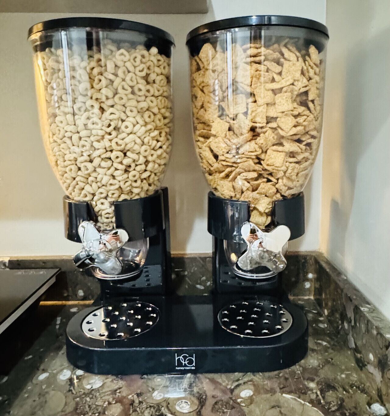 Two cylindrical dispensers on a kitchen counter, each filled with different types of cereal.