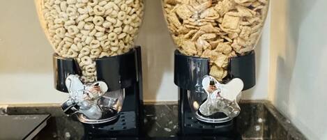 Two cylindrical dispensers on a kitchen counter, each filled with different types of cereal.