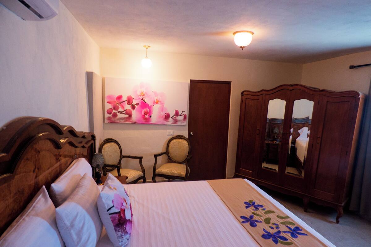 Une chambre à coucher avec un lit, deux chaises, une armoire et un tableau au mur.
