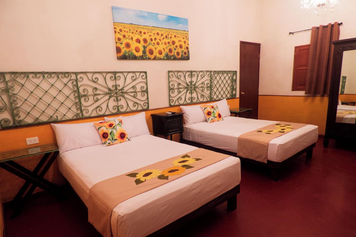 Une chambre d’hôtel avec deux lits, un tableau représentant des tournesols accroché au mur et une tête de lit en métal.