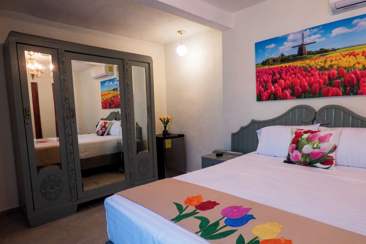 Une chambre à coucher avec un lit, une table de chevet, un miroir et un tableau représentant des tulipes.