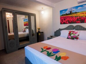 A bedroom with a bed, a nightstand, a mirror, and a painting of tulips. - Hotel Boutique Flores y Gemas (Mérida)