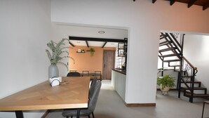 Un comedor moderno con una mesa y sillas de madera, una planta en maceta y una escalera con barandilla de metal.