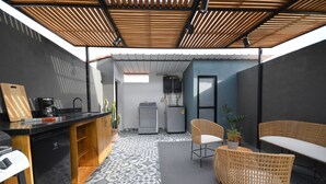 Cocina compacta con cafetera, refrigerador y zona de comedor con sillas de mimbre.