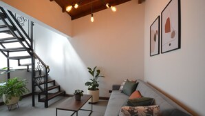 Una sala de estar moderna con una escalera, un sofá y dos cuadros abstractos enmarcados.