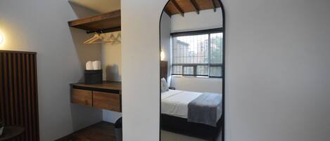 A bedroom with a bed, a wooden dresser, a mirror, and a window.