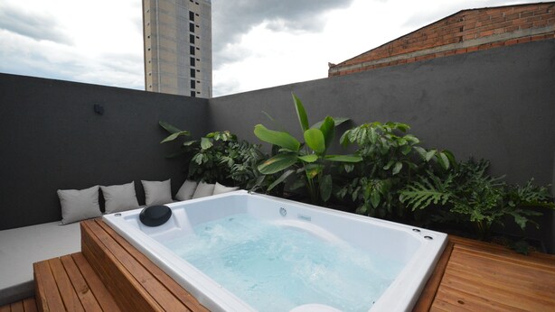 Un jacuzzi en la azotea con terraza de madera, rodeado de plantas verdes exuberantes y una pared gris.