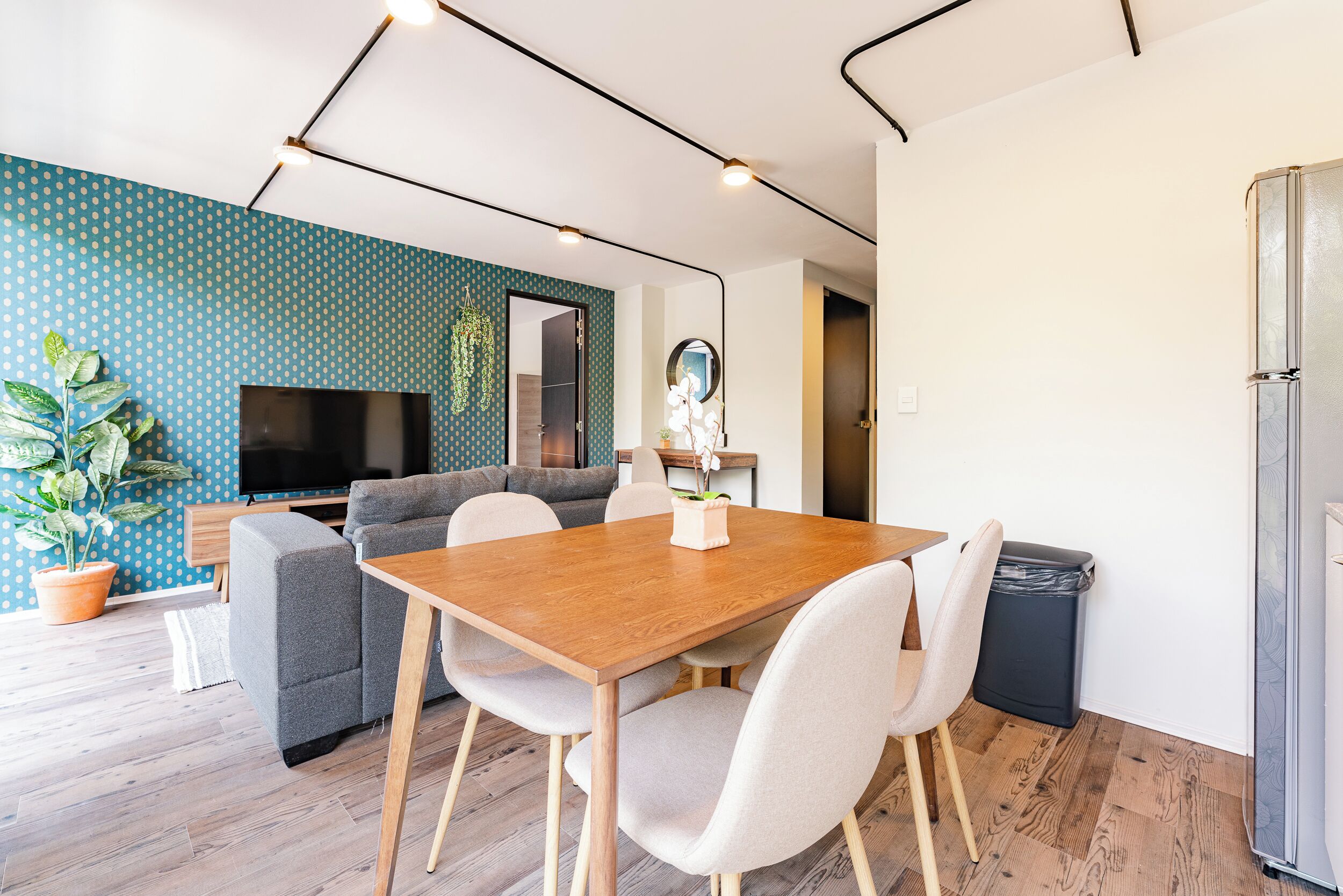 A modern living room with a wooden dining table, grey sofas, and a TV.