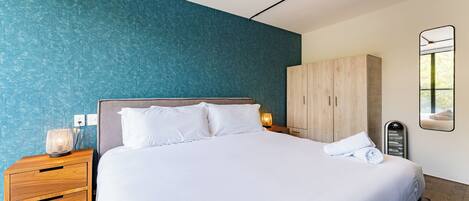 A modern bedroom with a large bed, wooden nightstand, and a wardrobe.